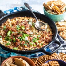 Cheesy bacon dip in a cast iron skillet surrounded by pretzels and crackers.