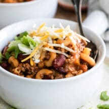 Chili mac topped with cheese, scallions and sour cream in a white bowl.