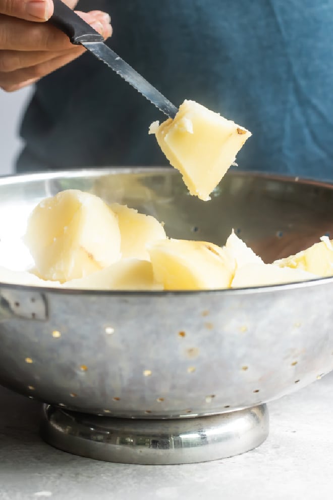 A sliced, boiled potato being held over a silver colander.