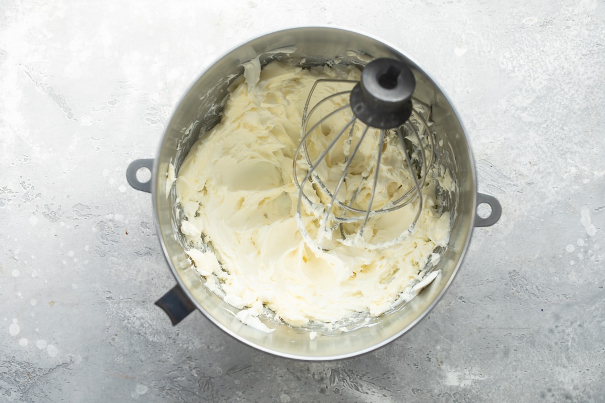 Cream cheese frosting being made in a silver mixing bowl.