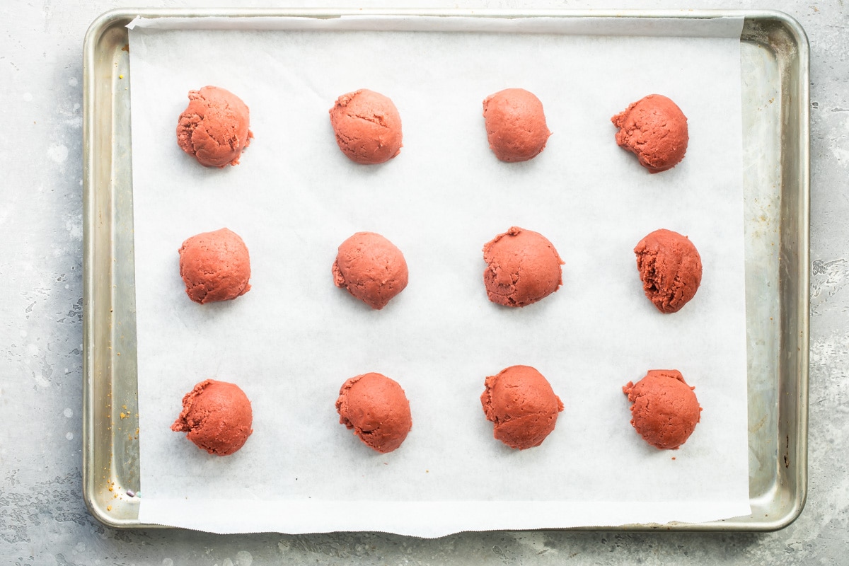 Balls of cookie dough on a parchment paper lined baking sheet.