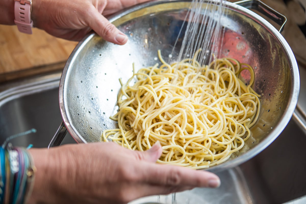 Pasta in a colander being rinsed over a sink.