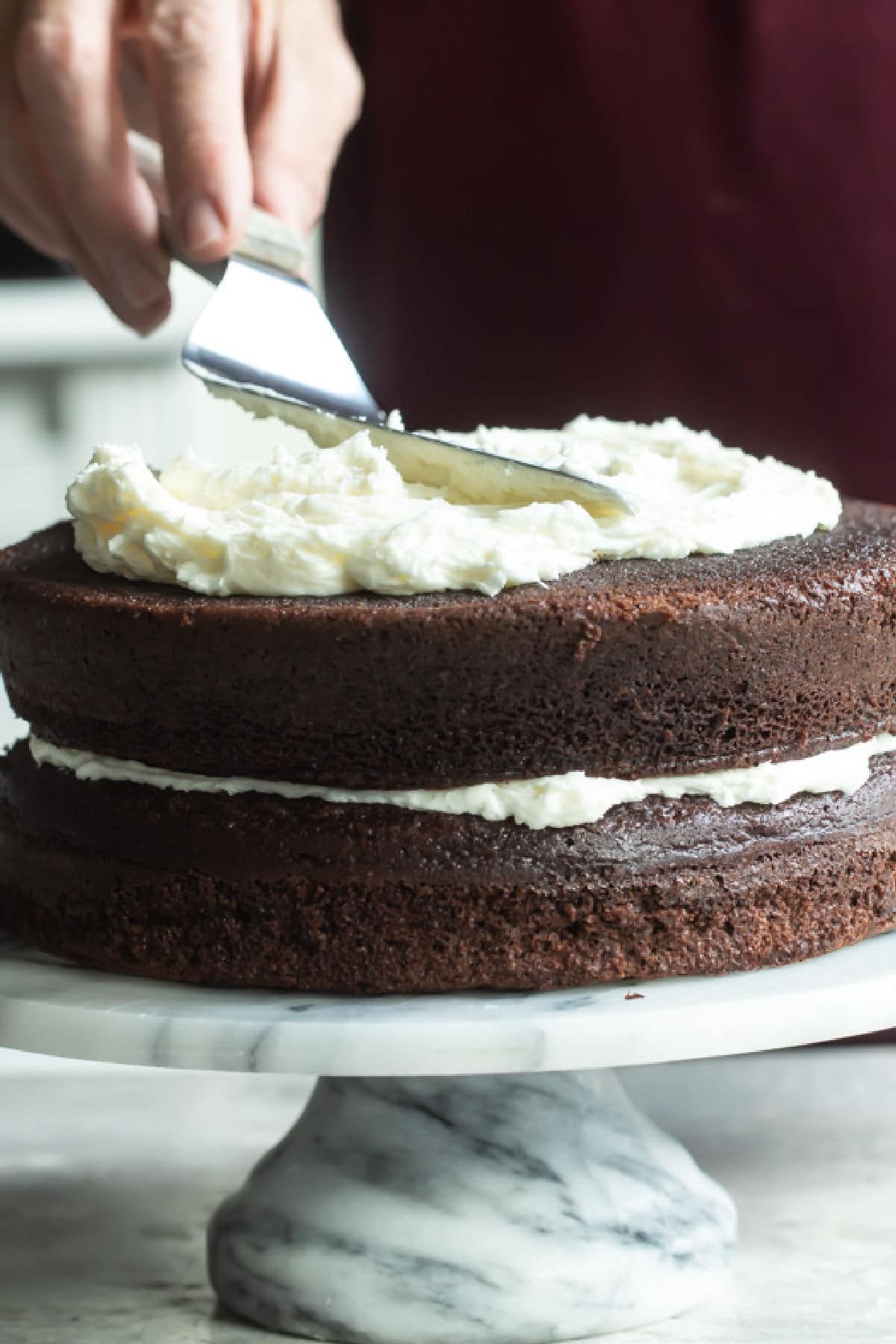 Buttercream frosting being spread on a chocolate layer cake.