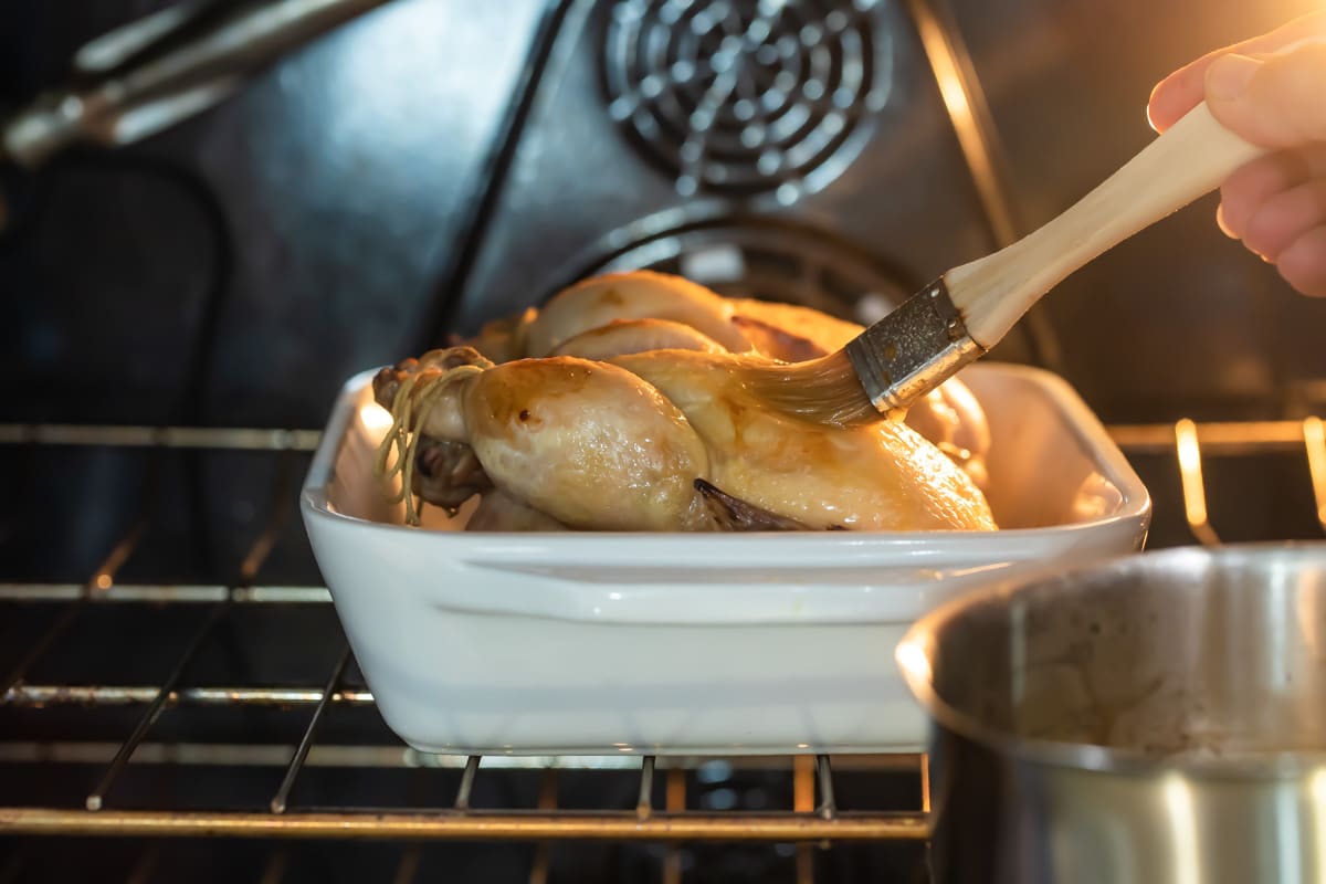 A Cornish hen in the oven being brushed with glaze.