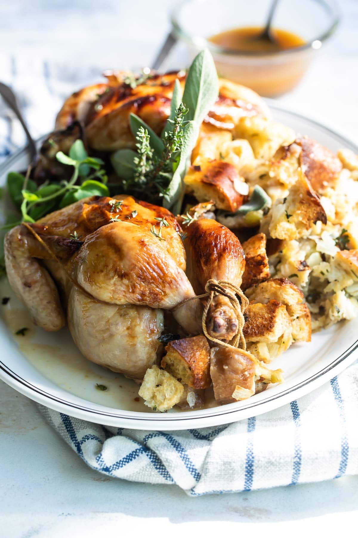 A whole Cornish hen on a gray plate with stuffing.