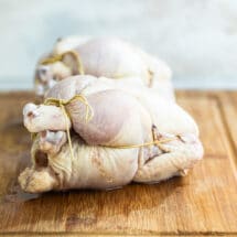 Two trussed Cornish hens on a wooden cutting board.