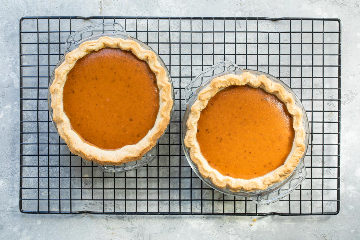 Two baked mini pumpkin pies on a cooling rack.
