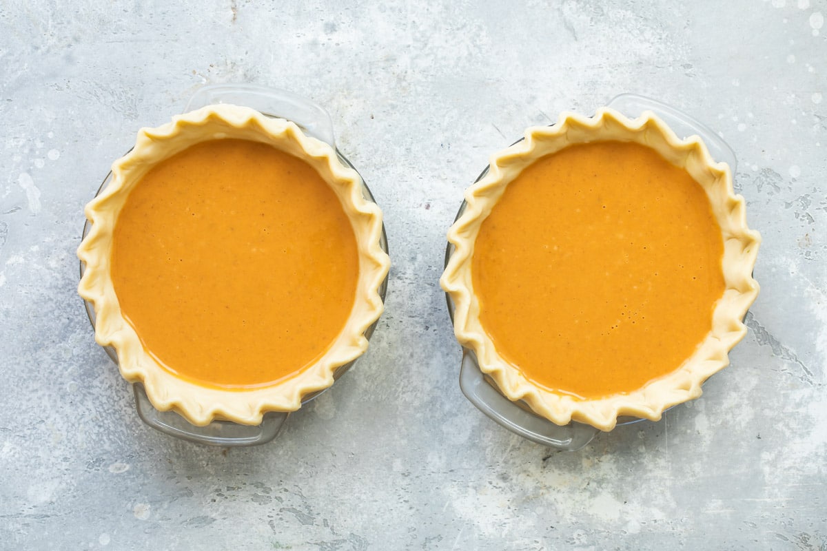 Two mini pumpkin pies on a counter before being baked.
