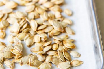 Pumpkin seeds on top of parchment paper on a baking sheet.