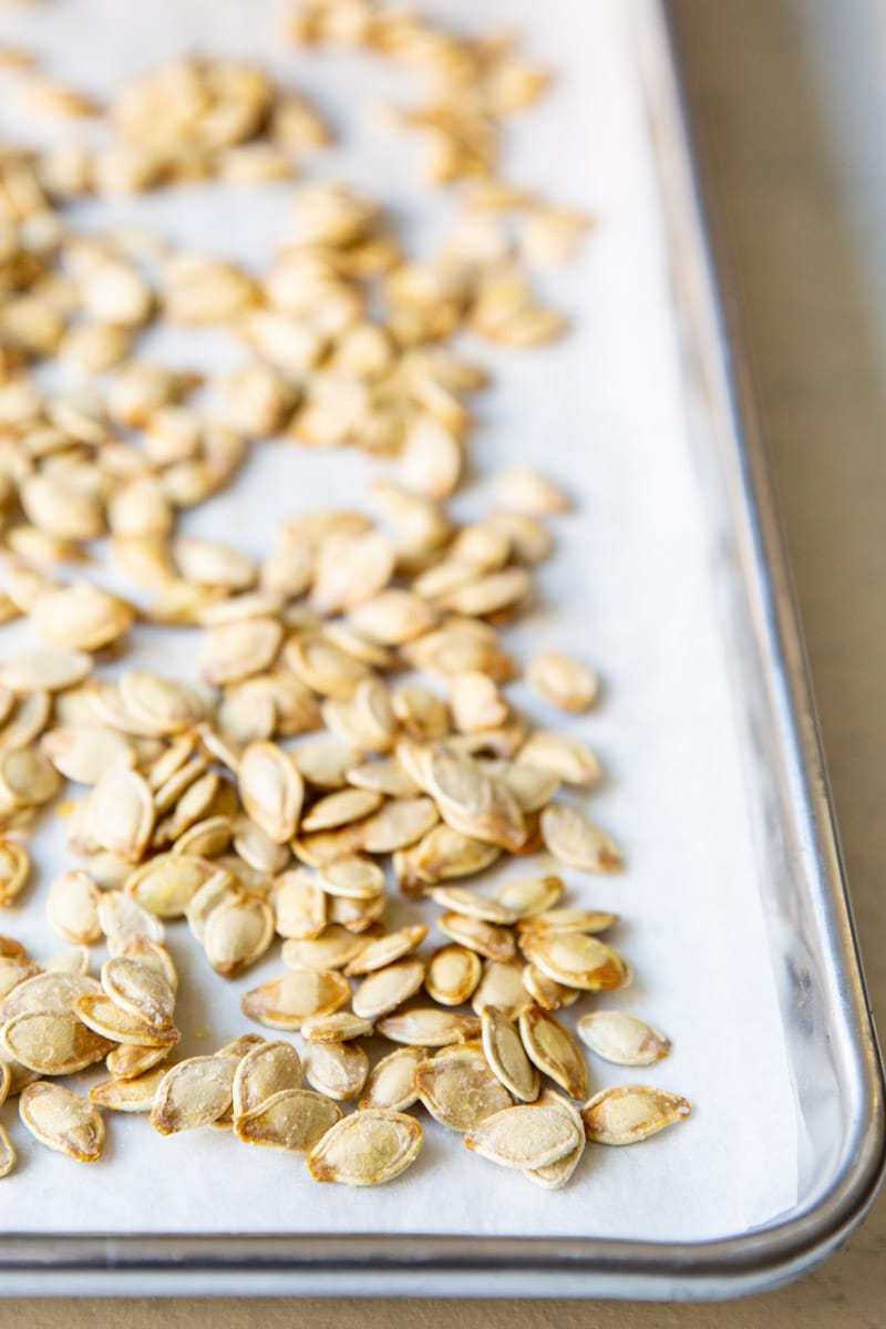 Pumpkin seeds on top of parchment paper on a baking sheet.