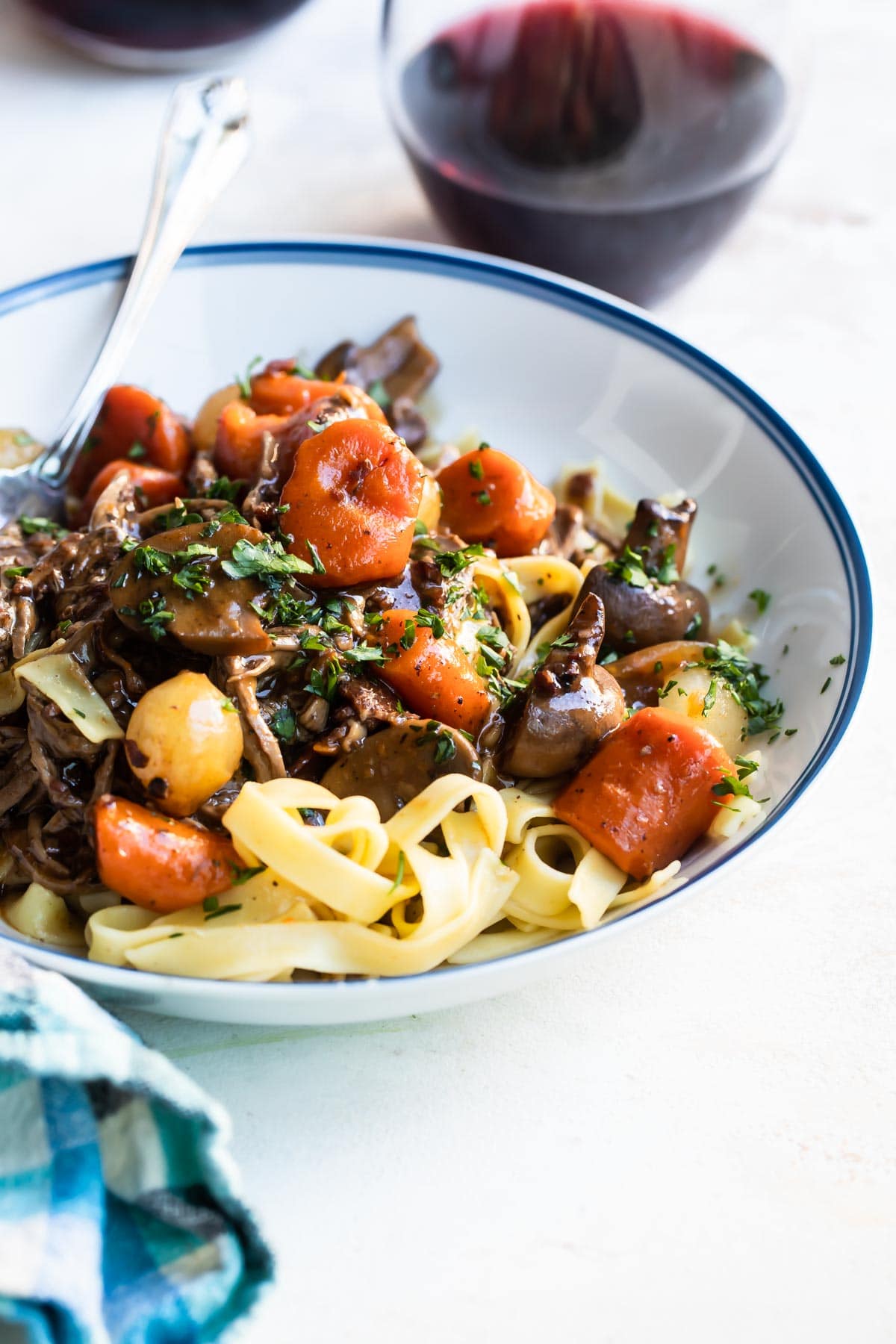 Beef Bourguignon over egg noodles in a white bowl.