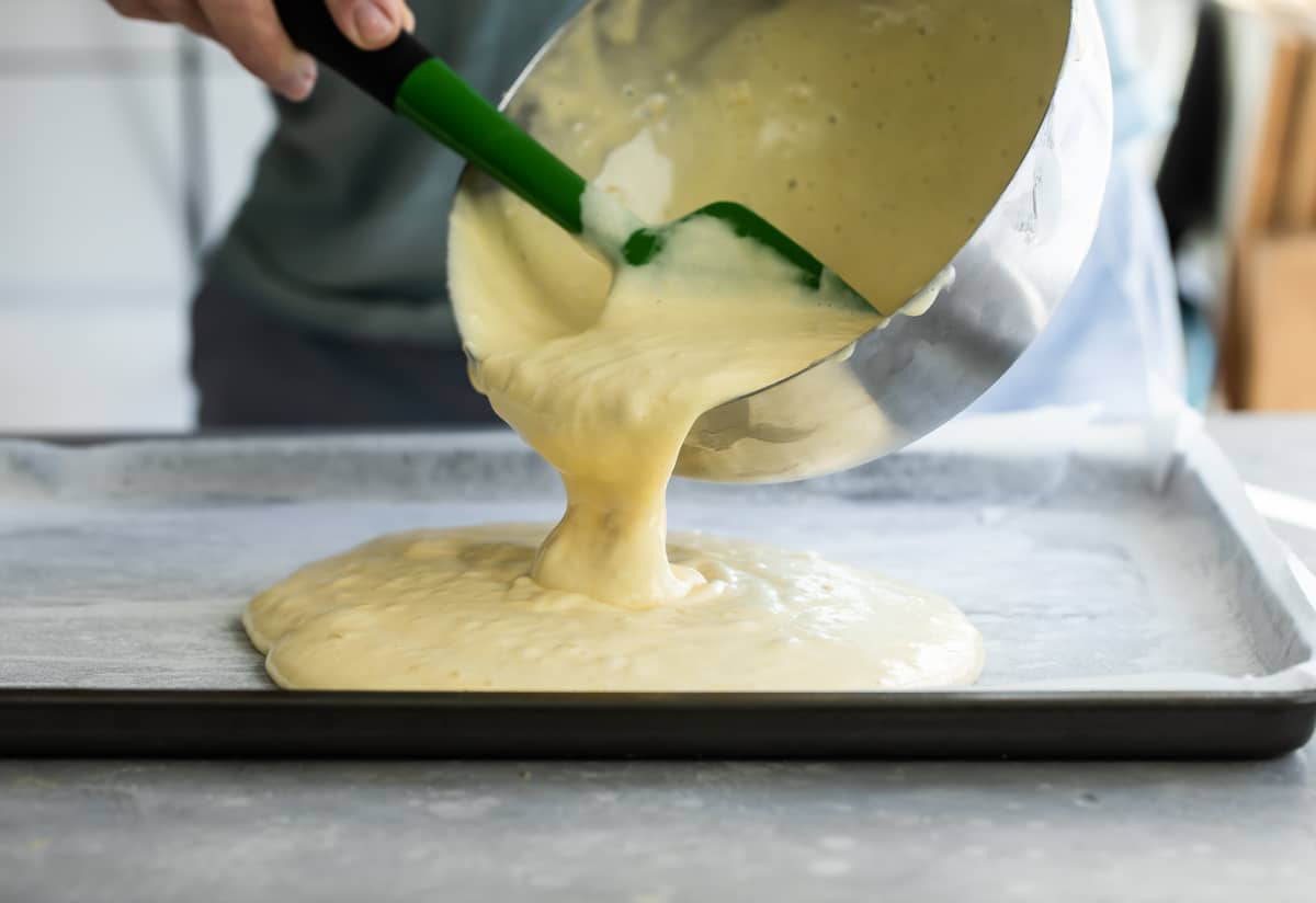 Cake batter being poured onto a jelly roll pan.