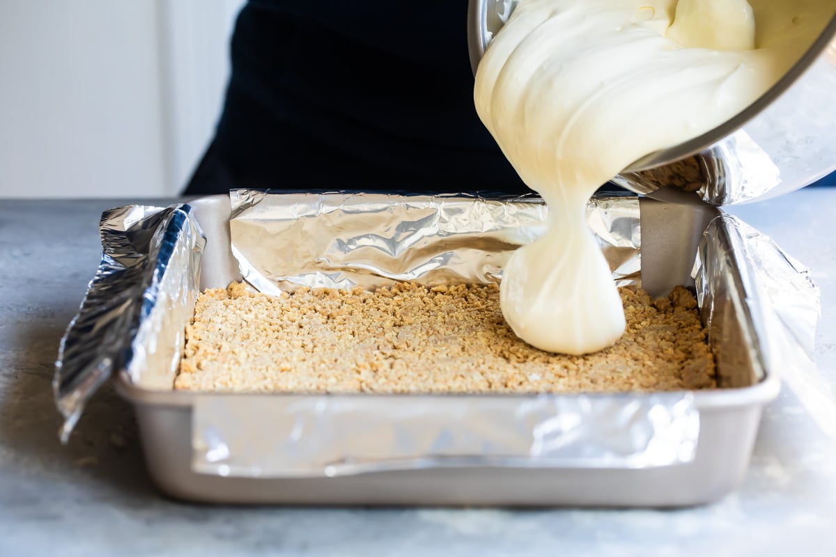 Pouring cheesecake filling over graham cracker crust.