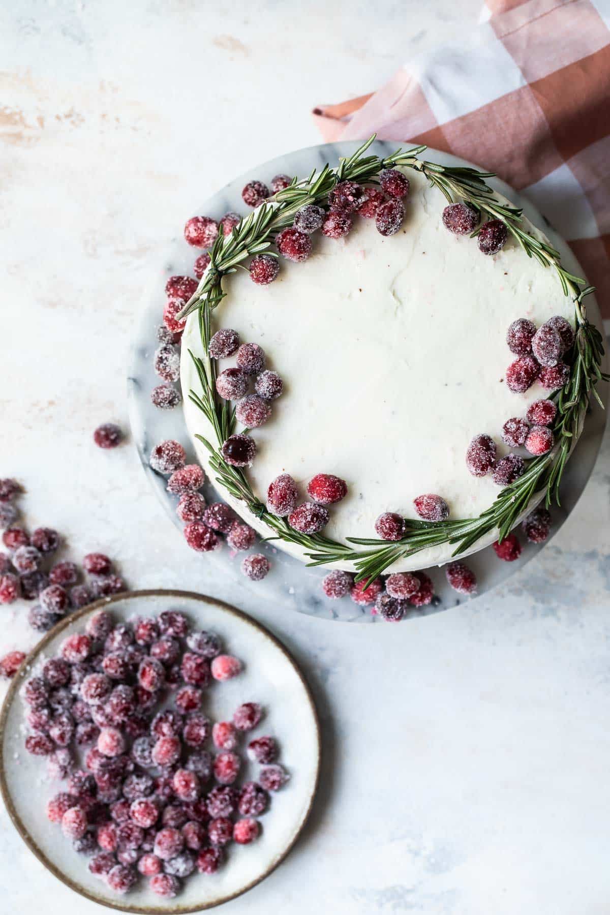 A cranberry wreath cake next to a plate of sugared cranberries.