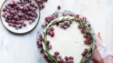 A cranberry wreath cake on a granite cake platter with a small plate of sugared cranberries next to it.