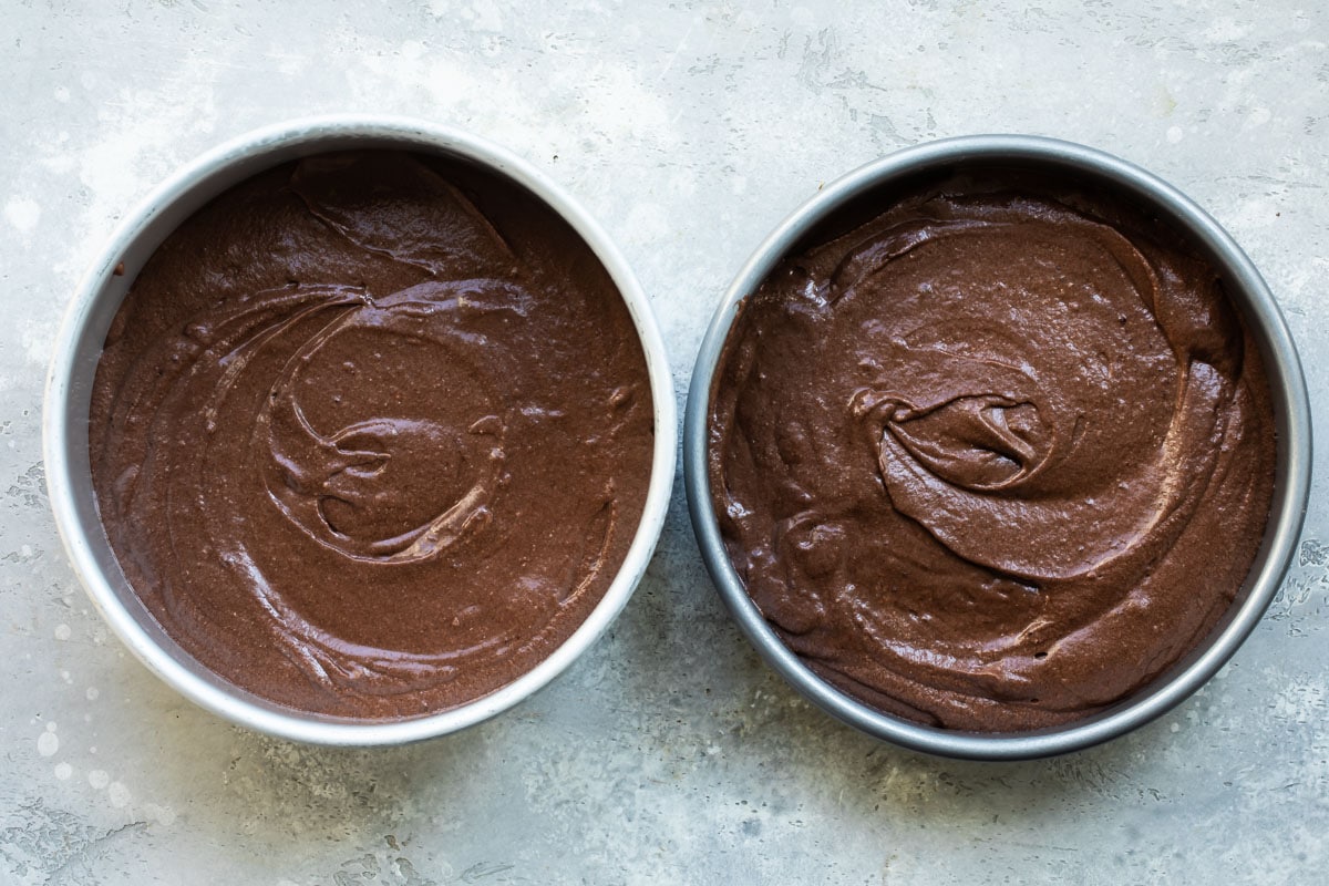 Round chocolate cakes in silver pans before being baked.