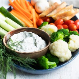 A platter with dill dip and fresh vegetables.