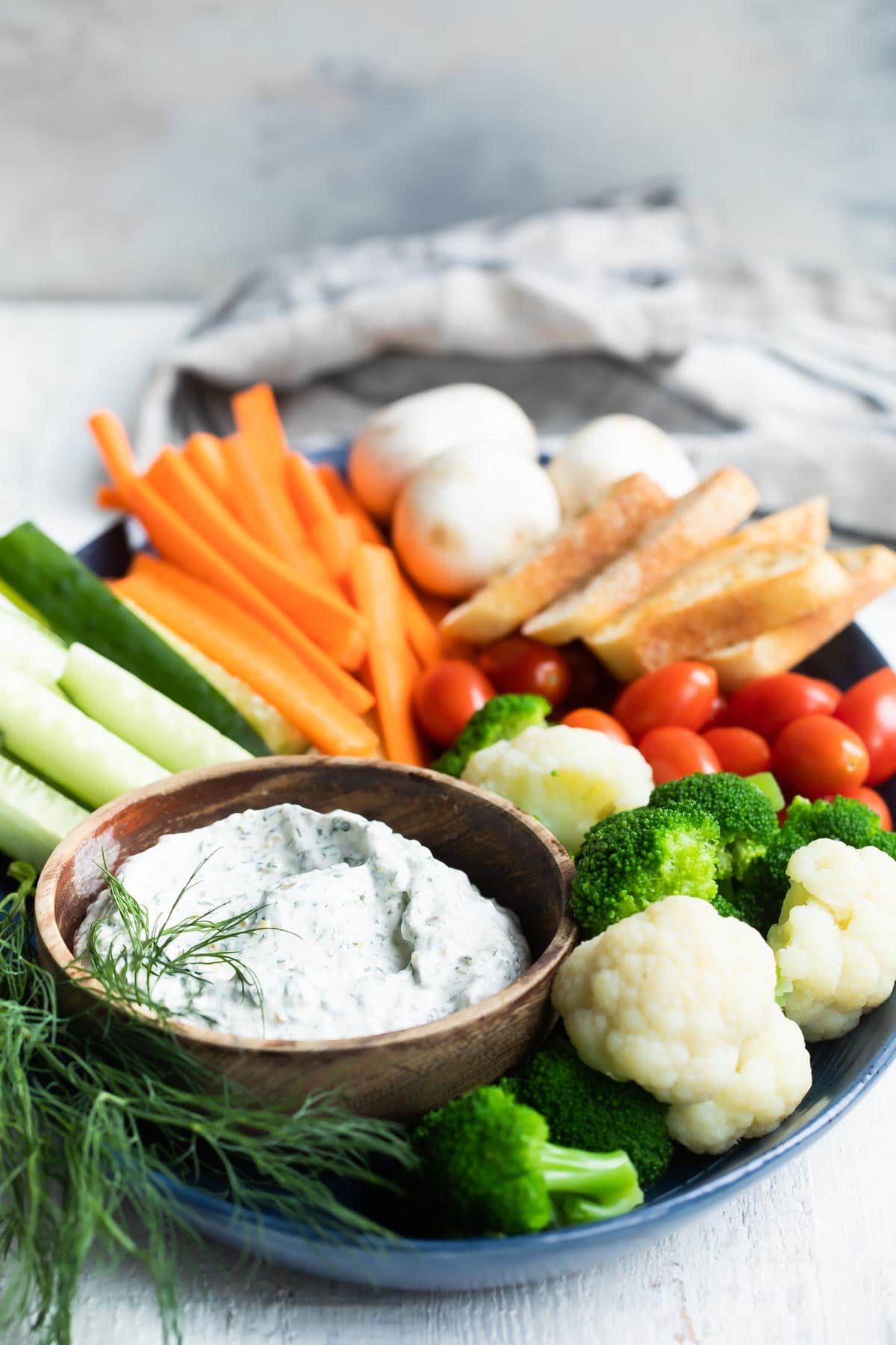 A platter with dill dip and fresh vegetables.