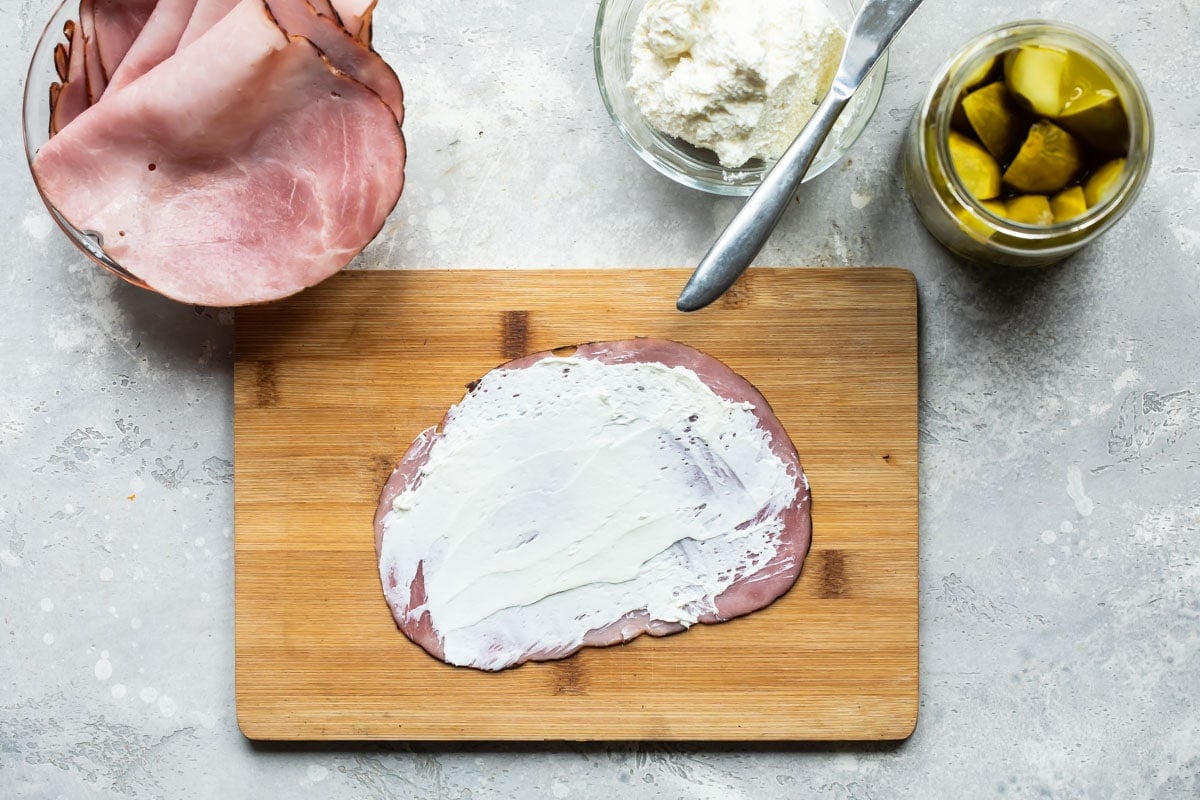 Ham roll ups being assembled on a cutting board.