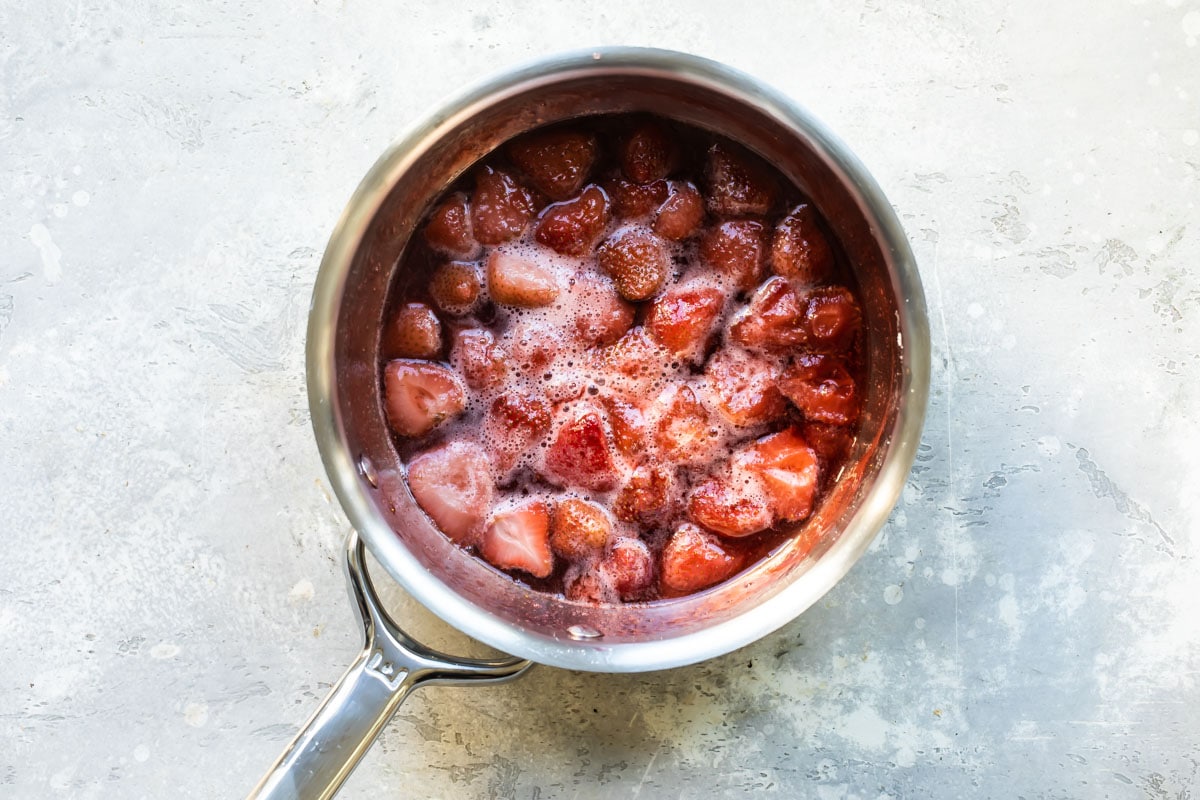 Frozen strawberries in a saucepan with water and sugar.