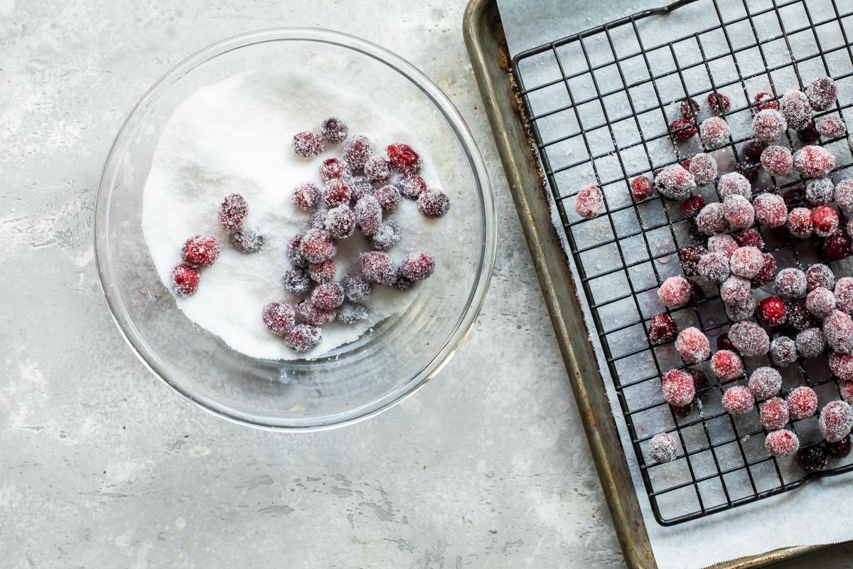 Cranberries in a bowl of sugar next to a cooling rack with cranberries on it.