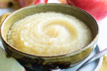 A bowl of applesauce with apples behind it.