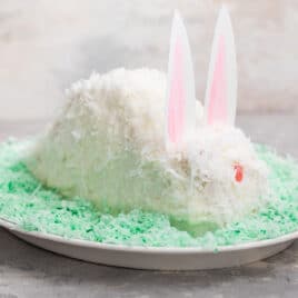 A bunny cake on a bed of green coconut on an oval plate.