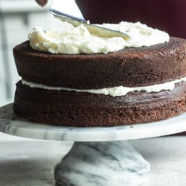 Buttercream frosting being spread on a chocolate layer cake.