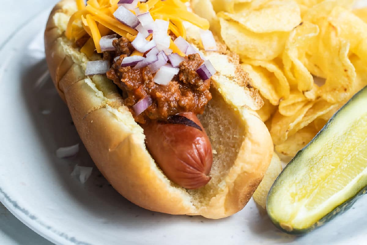 A chili dog on a plate with a pickle and chips.