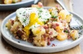 Corned beef hash on a gray plate topped with and egg and parsley.