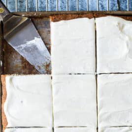 Banana bars with cream cheese frosting in a pan with a spatula for serving.