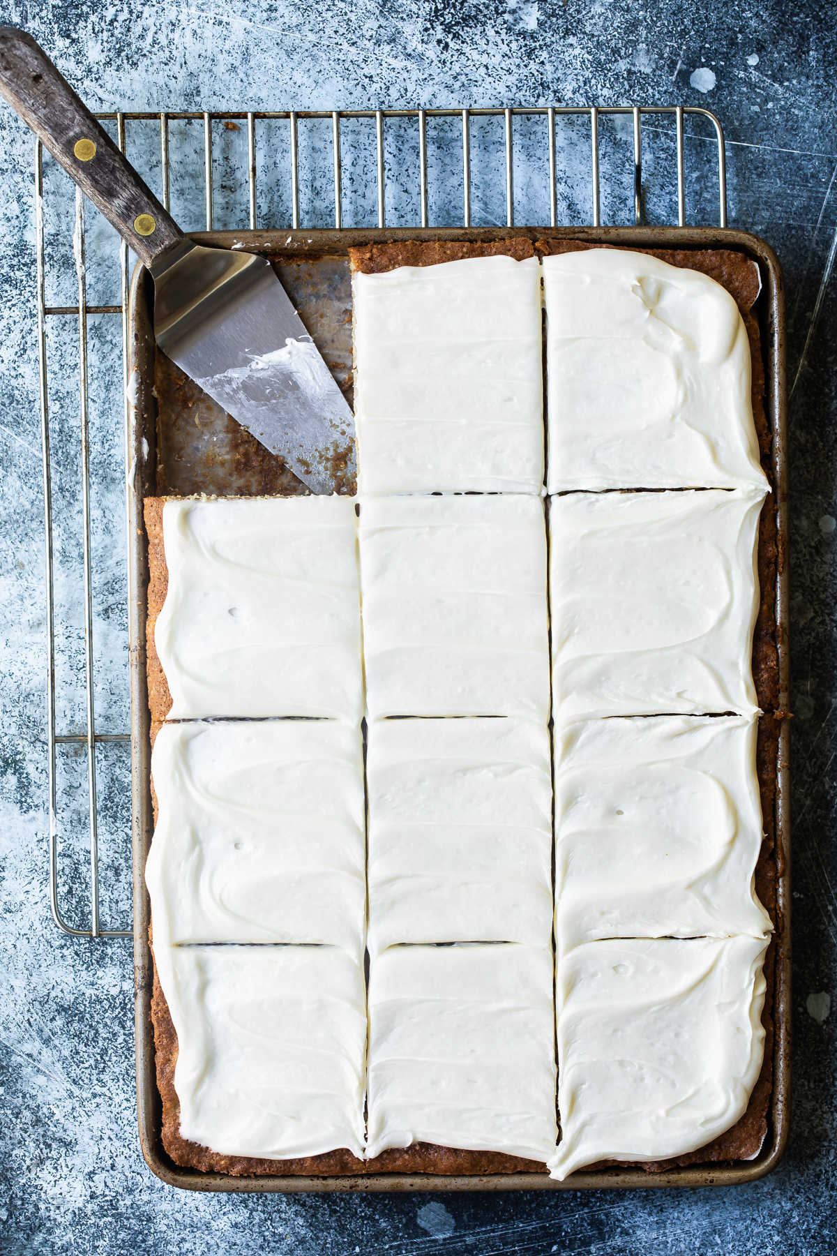 Banana bars with cream cheese frosting in a pan with a spatula for serving.