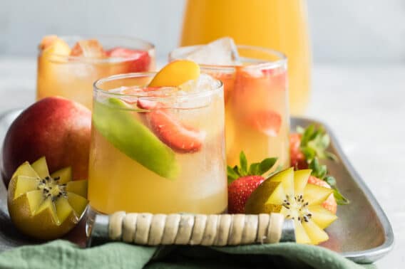 Passion fruit and pineapple sangria in three clear glasses on a silver platter.