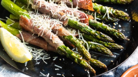 Prosciutto wrapped asparagus on a black plate with shredded Parmesan.