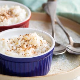 Rice pudding in two ramekins on a plate next to two spoons.