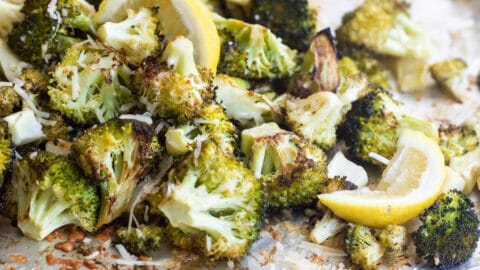 Roasted broccoli on a baking sheet with lemon garnish.