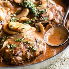 Salisbury steaks in a skillet with mushrooms, onions, and gravy.