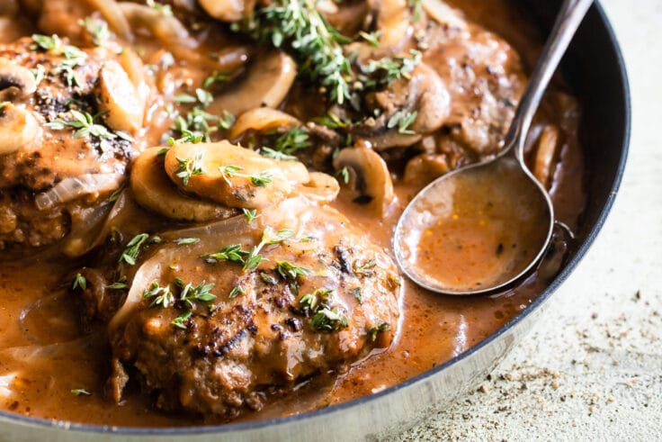 Salisbury steaks in a skillet with mushrooms, onions, and gravy.