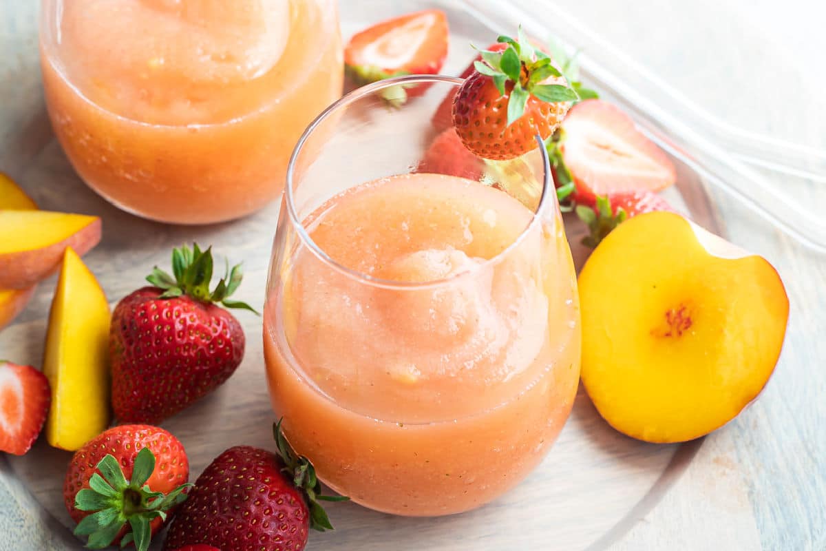 Two glasses of strawberry peach frose on a plate surrounded by slices of strawberries and peaches.
