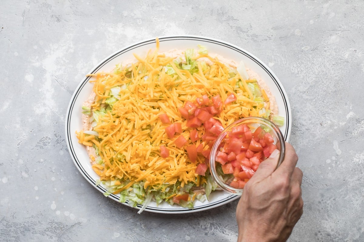 Someone putting tomatoes on top of layers of taco dip.