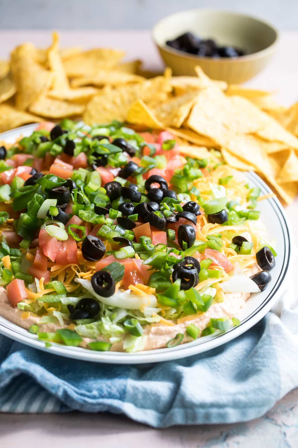 A platter of taco dip with tortilla chips in the background.