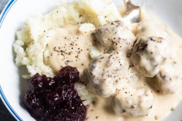 Swedish meatballs on plates with mashed potatoes, gravy, and cranberry sauce.