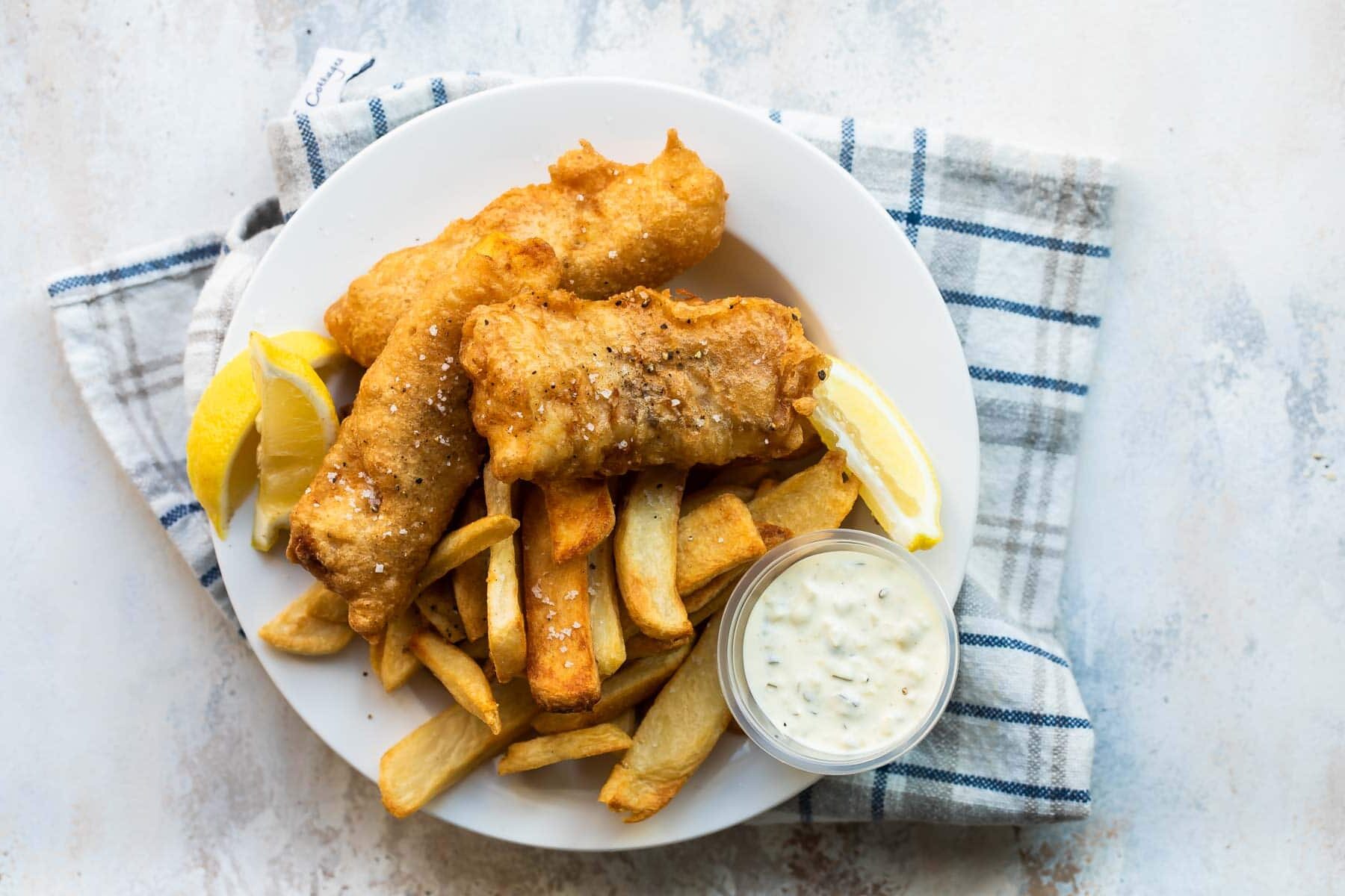 Beer battered cod, fries, tartar sauce and a lemon wedge on a plate.