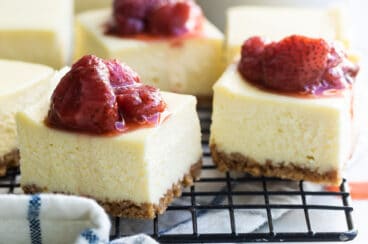 Cheesecake bars on a cooling rack topped with strawberry topping.