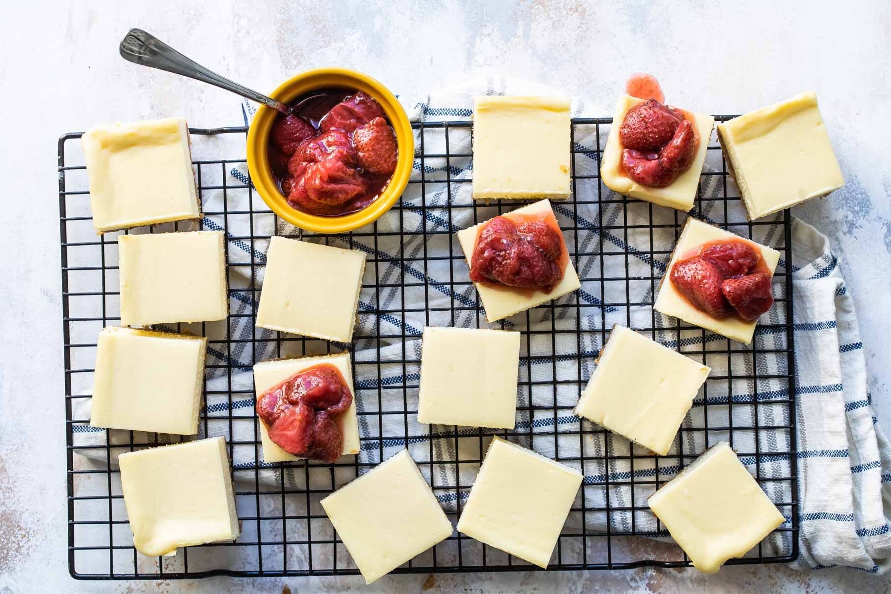 Cheesecake squares topped with strawberry topping on a cooling rack.