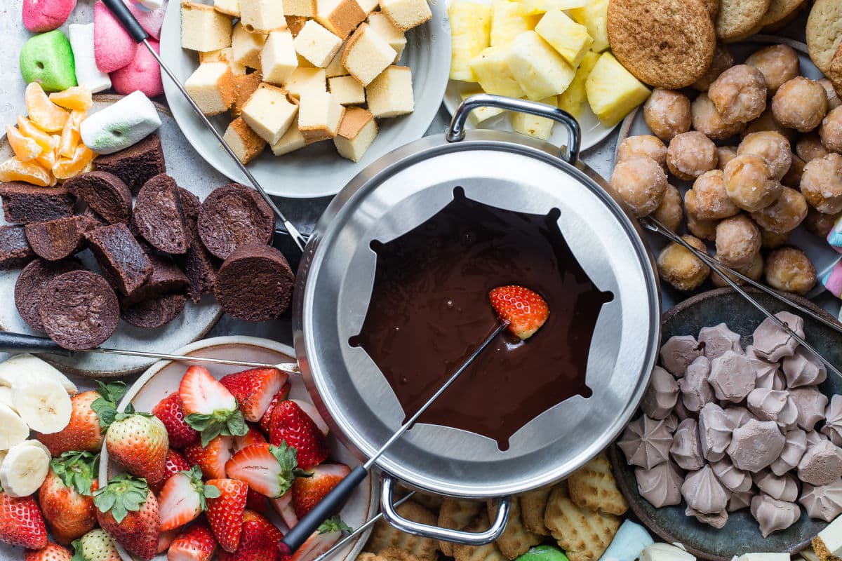 A platter of chocolate fondue and colorful dippers like fruit and sweets.
