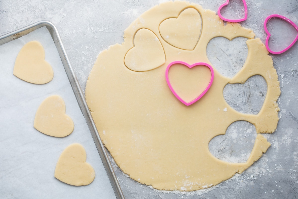 Dough for Easy Frosted Valentine cookies being cut with heart shaped cookie cutters.