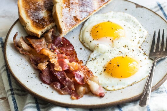 Sunny side up eggs on a plate with bacon and toast.
