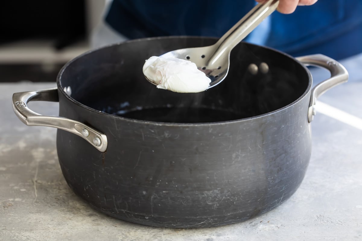 Lifting a poached egg out of a pot of water with a slotted spoon.