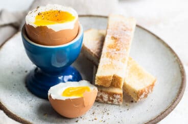 A soft boiled egg in a blue egg cup with toast sticks next to it.
